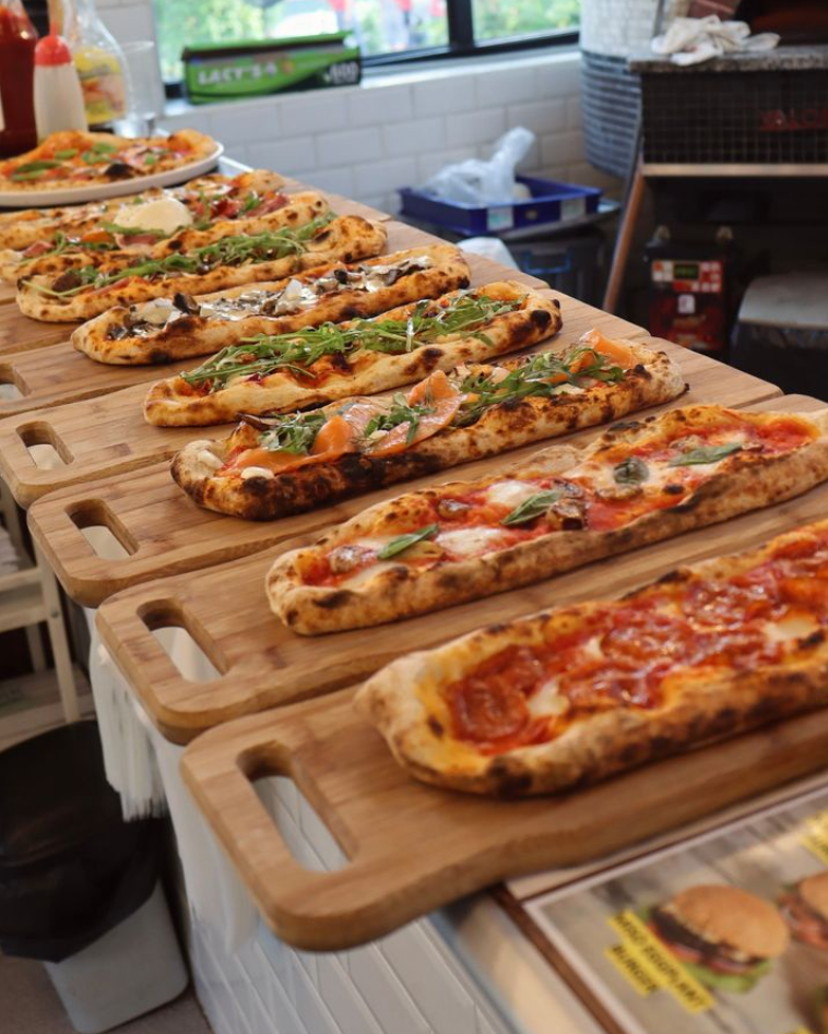 A row of pizzas on a table

Description automatically generated