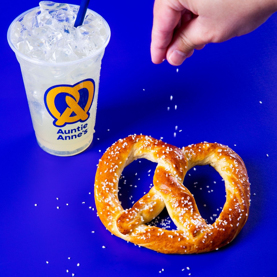 A hand sprinkling salt on a pretzel next to a cup of ice

Description automatically generated