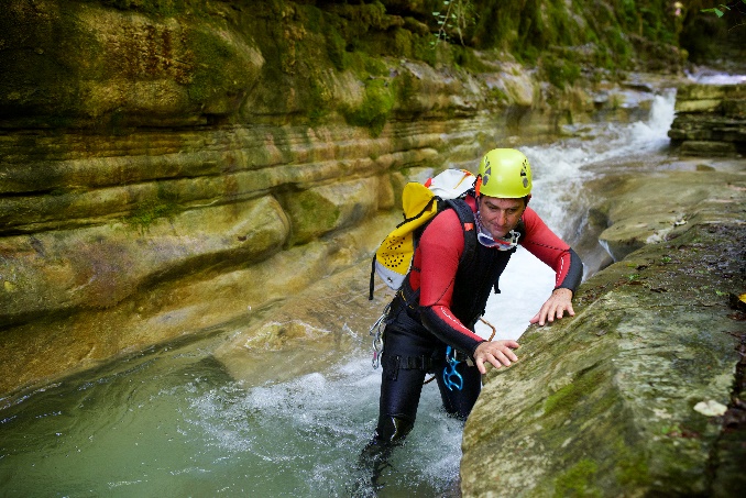 A person in a red shirt and yellow helmet climbing a rock

Description automatically generated